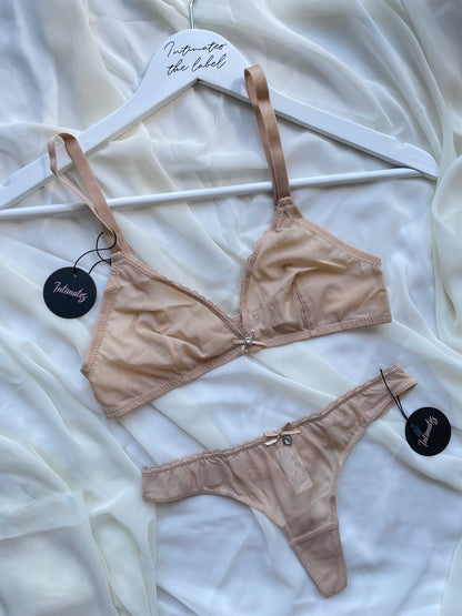 Beige bra and panties set on a hanger against a white fabric background.