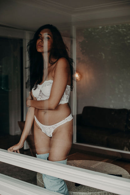 Woman in white lingerie standing in a room with a mirror reflection.