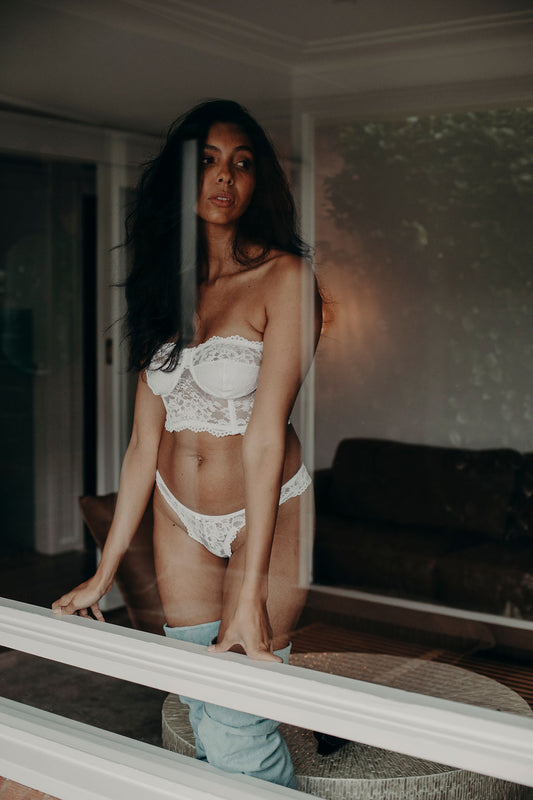 Woman in white lace lingerie standing in a room with a couch and mirror.
